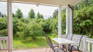 A covered patio with a table and chairs, surrounded by greenery and a view of the garden.