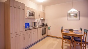 A compact kitchen with wooden cabinets, a microwave, a coffee maker, and a dining area with a table and chairs. - Comfort apartment with 1 bedroom and terrace on the first floor (Ostseebad Binz)