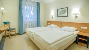 A hotel room with a double bed, a desk with a chair, a nightstand, and a window with curtains. - Comfort apartment with 1 bedroom and terrace on the first floor (Ostseebad Binz)