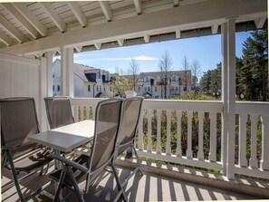 A covered outdoor patio with a table and chairs, a white railing, and a view of residential buildings. - Comfortable one-bedroom apartment with a balcony on the top floor (Ostseebad Binz)