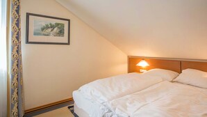 Ein Hotelzimmer mit einem großen Bett, einem Nachttisch mit Lampe, einem gerahmten Bild an der Wand und einem Fenster mit Vorhängen.