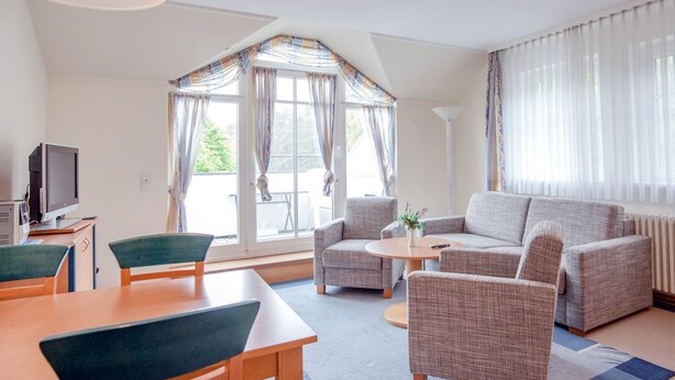 Ein modernes Wohnzimmer mit einer Couch, Sesseln, einem Esstisch und einem Fernseher.
