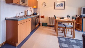 A compact kitchen with wooden cabinets, a microwave, a kettle, and a dining area with a table and chairs. - Budget Ferienwohnung mit 1 Schlafzimmer und Balkon im Dachgeschoss (Ostseebad Binz)