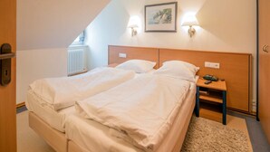 A bedroom with two beds, a wooden headboard, bedside lamps, a framed picture on the wall, and a radiator. - Budget Ferienwohnung mit 1 Schlafzimmer und Balkon im Dachgeschoss (Ostseebad Binz)