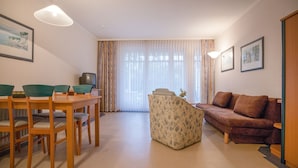 A living room with a wooden dining table, green chairs, a floral sofa, and a brown couch. - Classic apartment with 1 bedroom and terrace on the first floor (Ostseebad Binz)