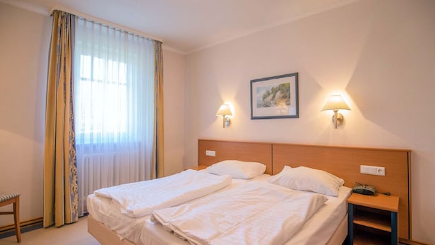 A double bed with white linens, two bedside tables, a nightstand, a framed picture on the wall, and a window with curtains. - Classic apartment with 1 bedroom and terrace on the first floor (Ostseebad Binz)