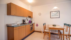 A compact kitchen with wooden cabinets, a built-in oven, and a dining area with a table and chairs. - Classic apartment with 1 bedroom and terrace on the first floor (Ostseebad Binz)