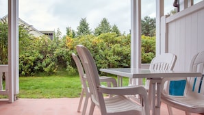 A patio with a table and chairs, a tiled floor, and a view of a garden with trees and bushes. - Classic apartment with 1 bedroom and terrace on the first floor (Ostseebad Binz)