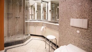 A modern bathroom with a glass-enclosed shower, a white toilet, and a small white stool.