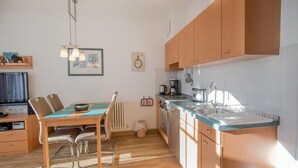 A modern kitchen with wooden cabinets, a dining table with chairs, a built-in oven, and a sink. - Comfort apartment with 1 bedroom and balcony on the top floor (Ostseebad Binz)