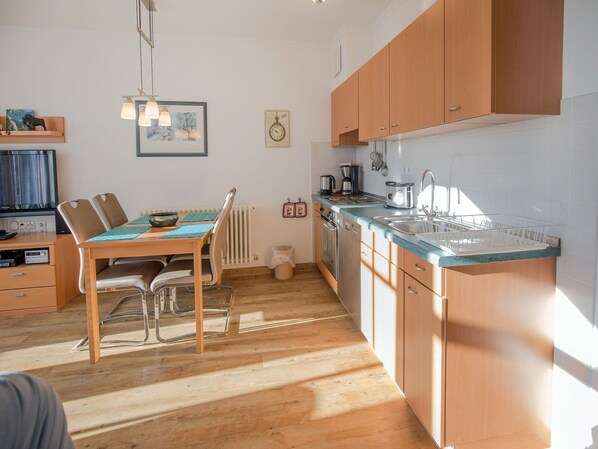 A modern kitchen with wooden cabinets, a dining table with chairs, a built-in oven, and a sink. - Comfort apartment with 1 bedroom and balcony on the top floor (Ostseebad Binz)