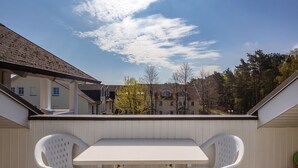A balcony with a white table and two white chairs, overlooking a residential area with houses and trees. - Comfort apartment with 1 bedroom and balcony on the top floor (Ostseebad Binz)