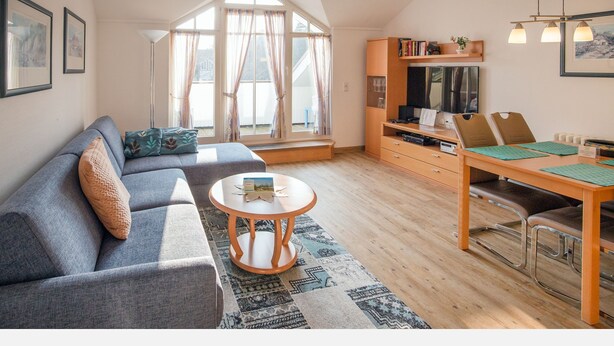 A cozy living room with a sofa, a coffee table, and a dining area with chairs and a table. - Comfort apartment with 1 bedroom and balcony on the top floor (Ostseebad Binz)