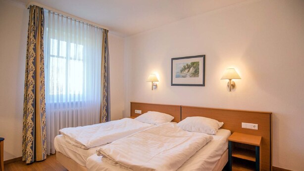 Una cama doble con dos mesitas de noche, un cuadro en la pared y una ventana con cortinas.