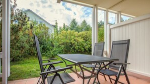 Un patio con mesa y sillas, rodeado de un jardín y una cerca blanca.