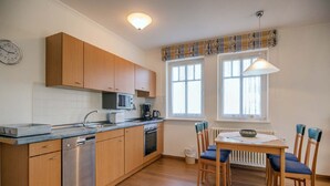 Cocina compacta con armarios de madera, microondas, cafetera y comedor con mesa y sillas.