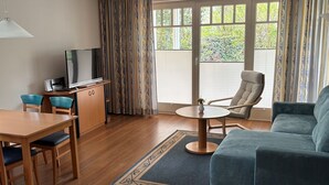 Una habitación con una mesa de comedor, sillas, un sofá, un televisor y un ventanal con cortinas.
