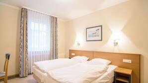 A hotel room with a double bed, a bedside table, a chair, a window with curtains, and a framed picture on the wall. - Comfort apartment with 1 bedroom and balcony on the upper floor (Ostseebad Binz)