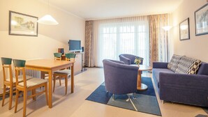 A modern living room with a dining area, a sofa, and a TV. - Comfort apartment with 1 bedroom and balcony on the upper floor (Ostseebad Binz)