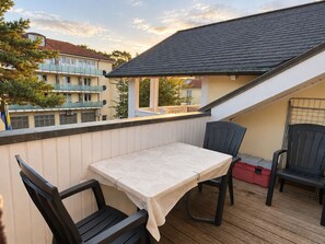 Un balcon avec une table et des chaises, une boîte de rangement rouge et une vue sur les immeubles voisins.