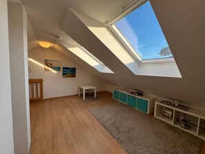 Une pièce avec des plafonds inclinés, des fenêtres de toit, une petite table blanche, des meubles de couleur turquoise et un plancher en bois.