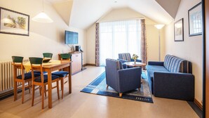 A modern living room with a dining area, a sofa, a TV, and a radiator. - Comfort apartment with 1 bedroom and balcony on the top floor (Ostseebad Binz)