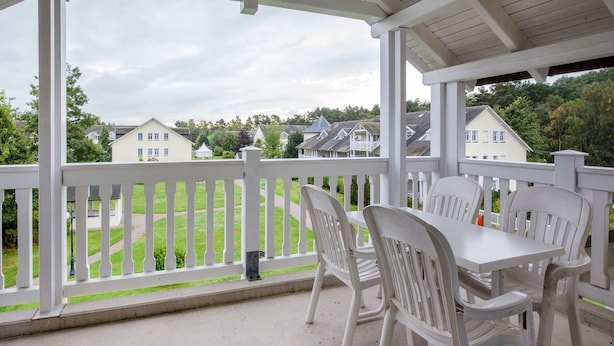 A covered patio with white chairs and a table, overlooking a green lawn and houses. - Comfort apartment with 1 bedroom and balcony on the top floor (Ostseebad Binz)