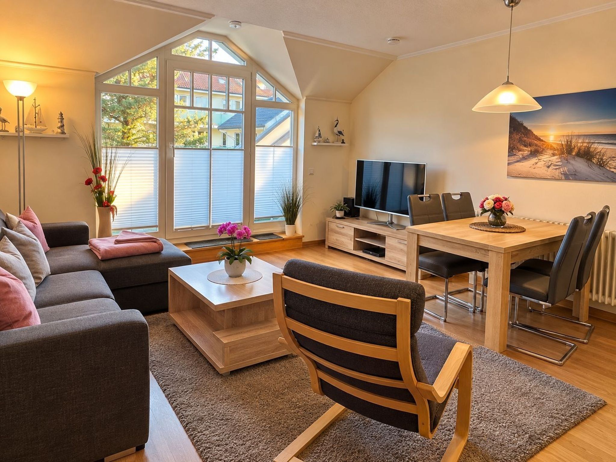 A modern living room with a sofa, coffee table, and a TV. There is a dining area with a table and chairs.
