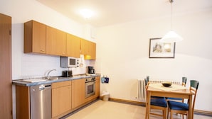 A compact kitchen with wooden cabinets, a microwave, a stove, and a dining area with a table and chairs. - Comfort apartment with 1 bedroom and balcony on the top floor (Ostseebad Binz)