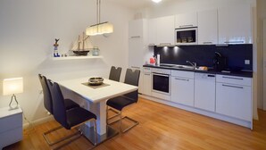 A modern kitchen with white cabinets, a black countertop, and a dining area with a white table and black chairs. - Comfort plus apartment with 1 bedroom and balcony on the upper floor (Ostseebad Binz)