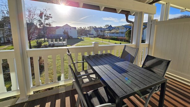 A covered outdoor patio with a wooden table and chairs, overlooking a residential area with houses and a lawn. - Comfort plus apartment with 1 bedroom and balcony on the upper floor (Ostseebad Binz)