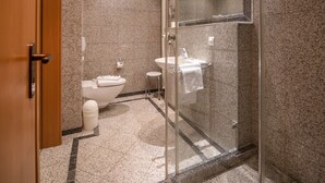 A modern bathroom with a glass shower enclosure, a toilet, a sink, and a bidet.