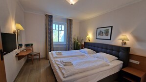 A hotel room with a bed, bedside tables, a desk with a chair, a television, and a window with curtains.