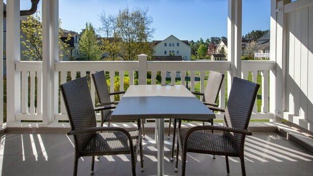 A covered patio with a table and chairs, white railings, and a view of houses in the background.