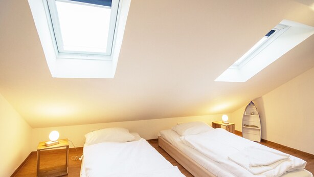 Een kleine, lichte kamer met twee bedden, een dakraam en een houten vloer.