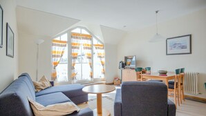 Een moderne woonkamer met een bank, fauteuils, een salontafel en een eethoek met een tafel en stoelen.