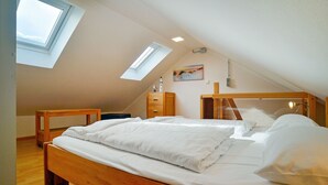 A bedroom with a wooden bed, two bedside tables, a nightstand, a skylight, and a painting on the wall. - Comfort plus apartment with 1 bedroom and balcony on the top floor (Ostseebad Binz)