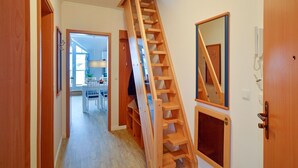 A wooden staircase in a hallway with a dining area in the background. - Comfort plus apartment with 1 bedroom and balcony on the top floor (Ostseebad Binz)