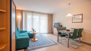 A modern hotel room with a sofa, a dining table with chairs, a TV, and a painting on the wall. - Comfort apartment with 1 bedroom and terrace on the first floor (Ostseebad Binz)