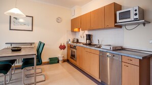 A modern kitchen with wooden cabinets, stainless steel appliances, a dining area with a table and chairs, and a hanging light fixture. - Comfort apartment with 1 bedroom and terrace on the first floor (Ostseebad Binz)