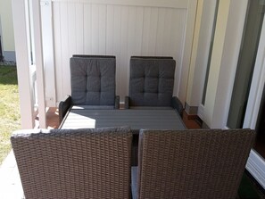 A patio with two grey cushioned chairs and a wicker table. - Comfortplus vacation apartment with 1 bedroom and terrace on the first floor (Ostseebad Binz)
