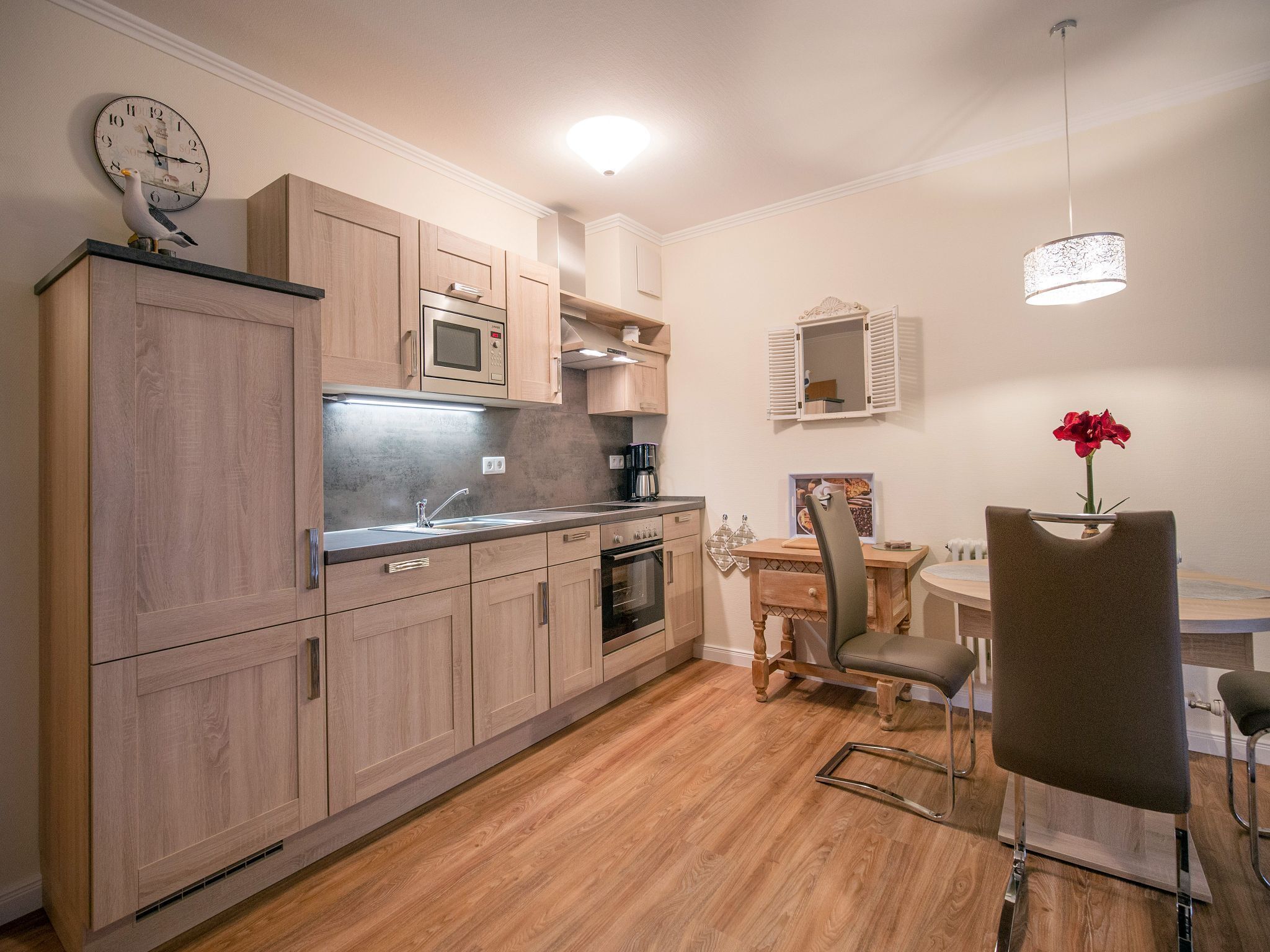 A modern kitchen with wooden cabinets, a built-in microwave, and a dining area with a table and chairs.