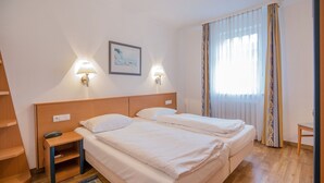 Ett hotellrum med två sängar, ett nattduksbord, en lampa, en inramad tavla på väggen och ett fönster med gardiner.