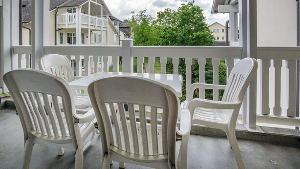 Ett takförsett utomhusområde med vita plaststolar och ett bord, med utsikt över ett bostadsområde med hus och ett grönt träd.