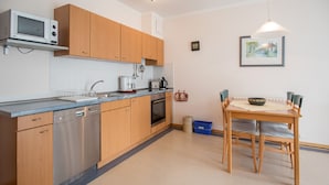 A modern kitchen with wooden cabinets, a built-in microwave, a dishwasher, and a dining area with a table and chairs. - Comfort apartment with 1 bedroom and balcony on the upper floor (Ostseebad Binz)