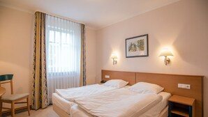 A hotel room with a double bed, two bedside lamps, a chair, a small table, and a painting on the wall. - Comfort apartment with 1 bedroom and balcony on the upper floor (Ostseebad Binz)