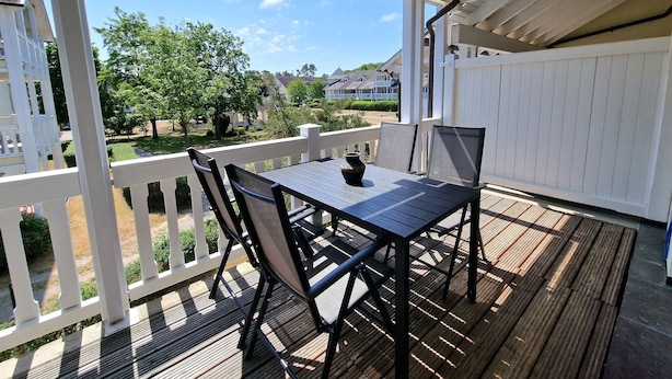 A covered outdoor patio with a table and chairs, a white fence, and a view of a residential area. - Comfort apartment with 1 bedroom and balcony on the upper floor (Ostseebad Binz)
