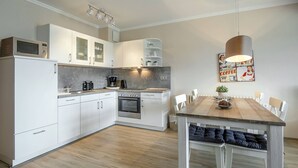 A modern kitchen with white cabinets, a wooden dining table, and a hanging light fixture.