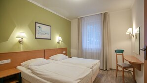 A hotel room with two beds, a desk, a chair, and a window with curtains. - Comfortplus vacation apartment with 1 bedroom and terrace on the first floor (Ostseebad Binz)