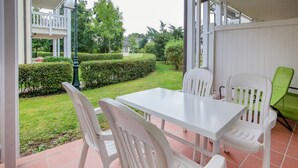 A patio with a white table and chairs, a green chair, and a view of a well-maintained garden and neighboring houses. - Comfortplus vacation apartment with 1 bedroom and terrace on the first floor (Ostseebad Binz)
